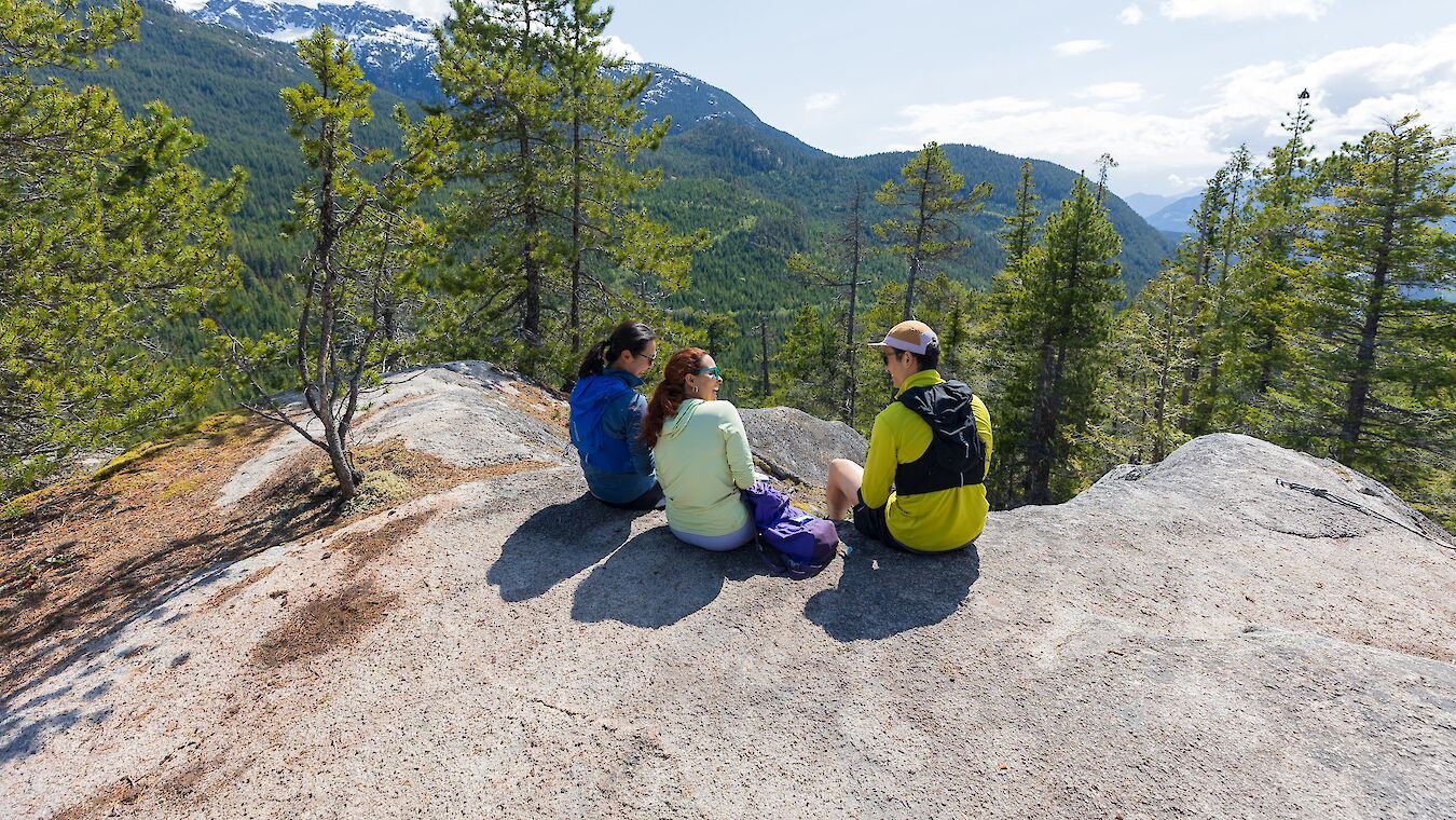 Three hikers sitting on a rock looking at the view
