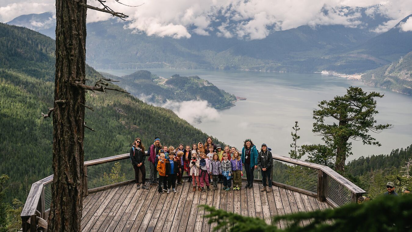 A group of students and teaches standing on the deck with a view behind