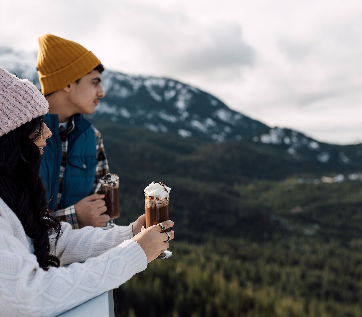 a brother and sister looking out at the view holding a hot chocolate