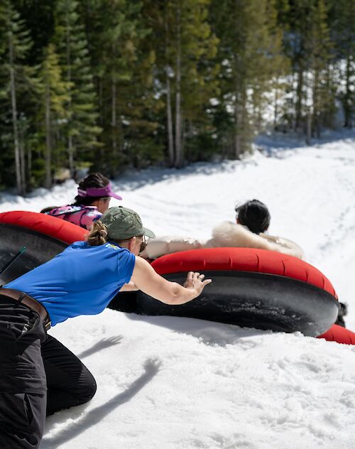 a girl pushing two people down the tube park on tubes