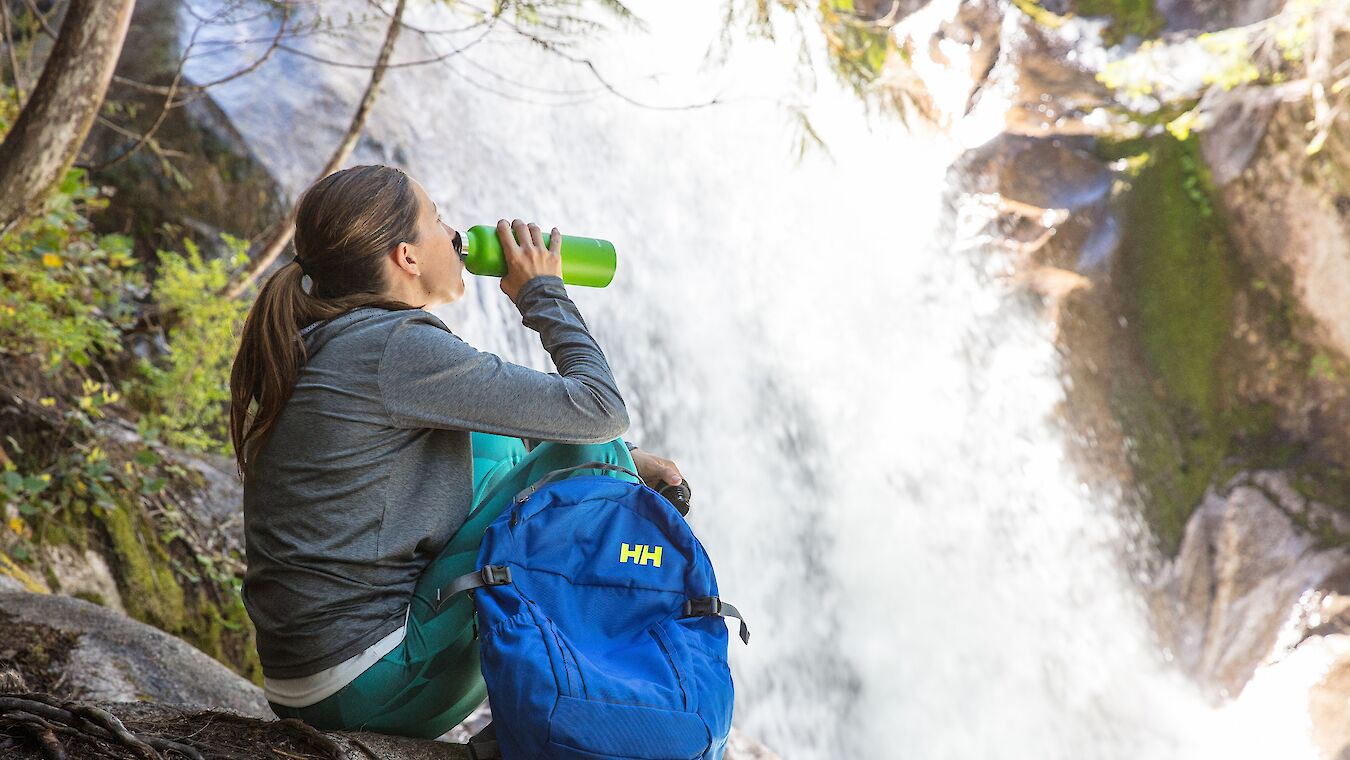 A women drinking out of a water bottle near a waterfall