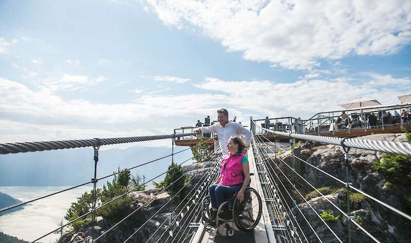 a man and women in a wheelchair on the suspension bridge looking at the veiw