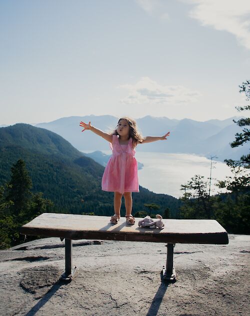 a little girl standing on a bench with an ocean view behind