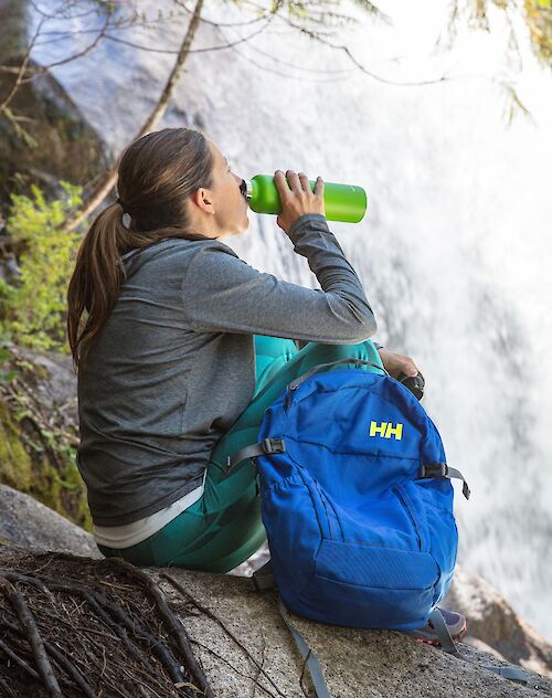 a women sitting drinking water next to a waterfall